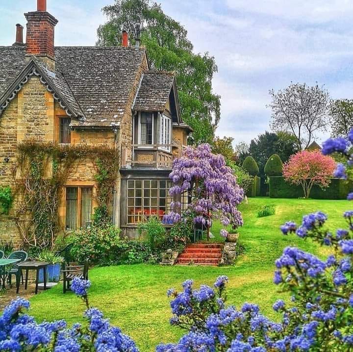 Stone cottage surrounded by colorful flowering plants and green lawn in an English country garden
