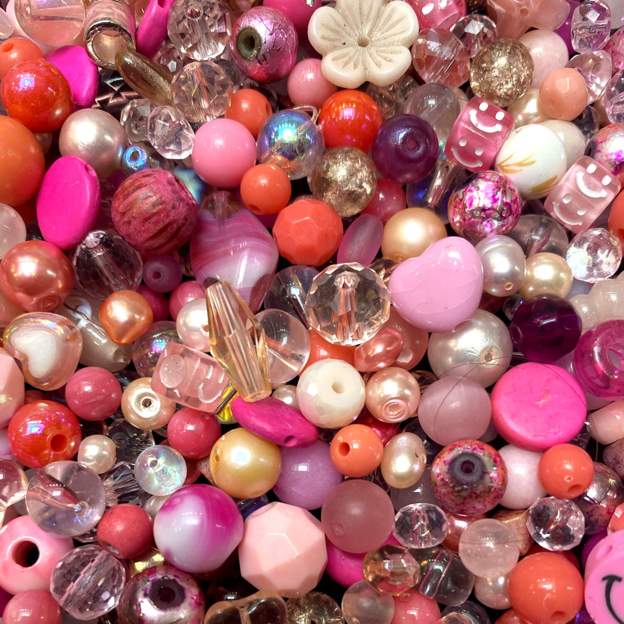 Overhead view of assorted colorful beads in pink, peach, purple, and silver tones densely packed together