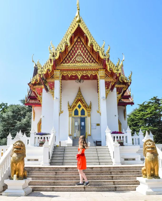 Woman in red dress posing in front of Buddhapadipa Thai temple with golden lion statues, Wimbledon