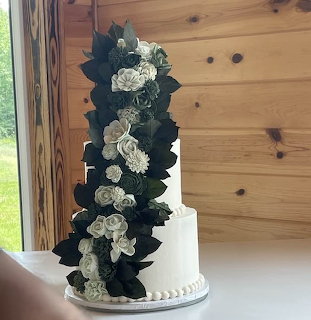 Tall white wedding cake with green leaves and white flowers cascading down the tiers
