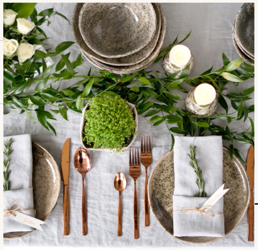 Overhead rustic table setting with plates, napkins, candles, greenery, and copper cutlery
