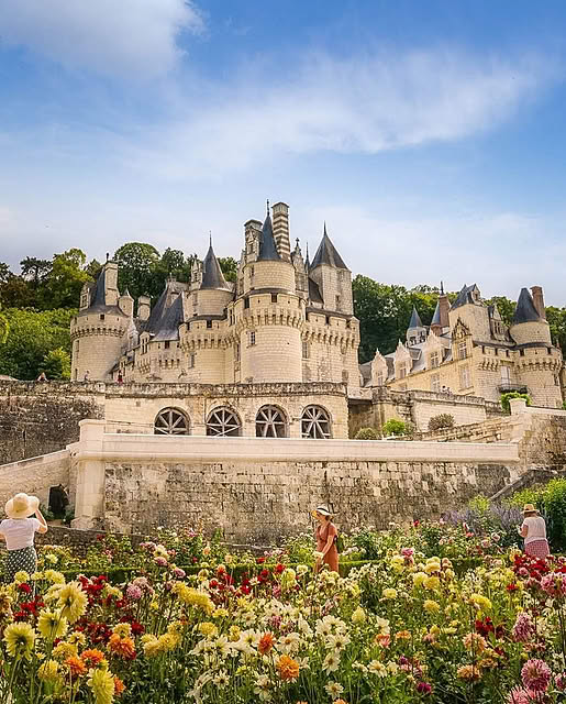 Château d'Ussé, a grand French castle with spires, surrounded by colorful blooming gardens under a blue sky.