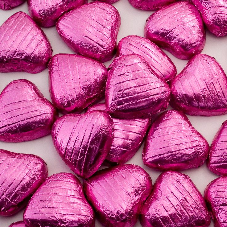 Pink foil-wrapped heart-shaped chocolates scattered on a light surface