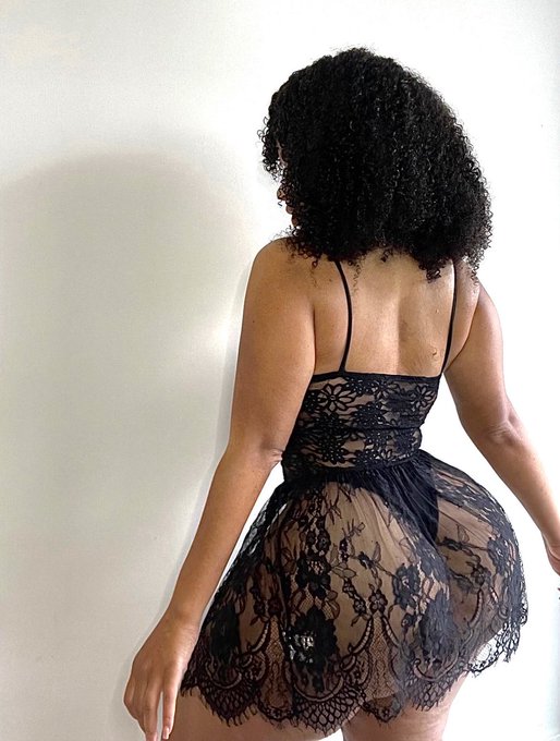 Woman with curly black hair posing from behind in sheer black lace lingerie