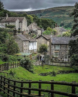Stone cottages in Castleton village with green hills and stormy sky above