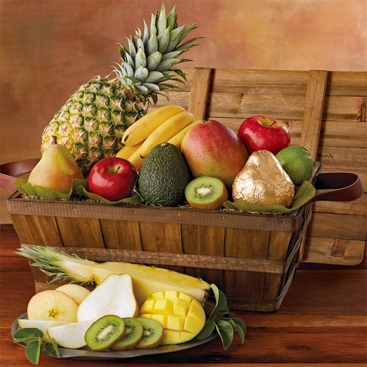 Wooden basket of assorted fresh fruit with sliced mango, pear, and kiwi on a table