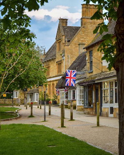 Traditional Cotswold stone buildings lining a village street with green lawn and trees