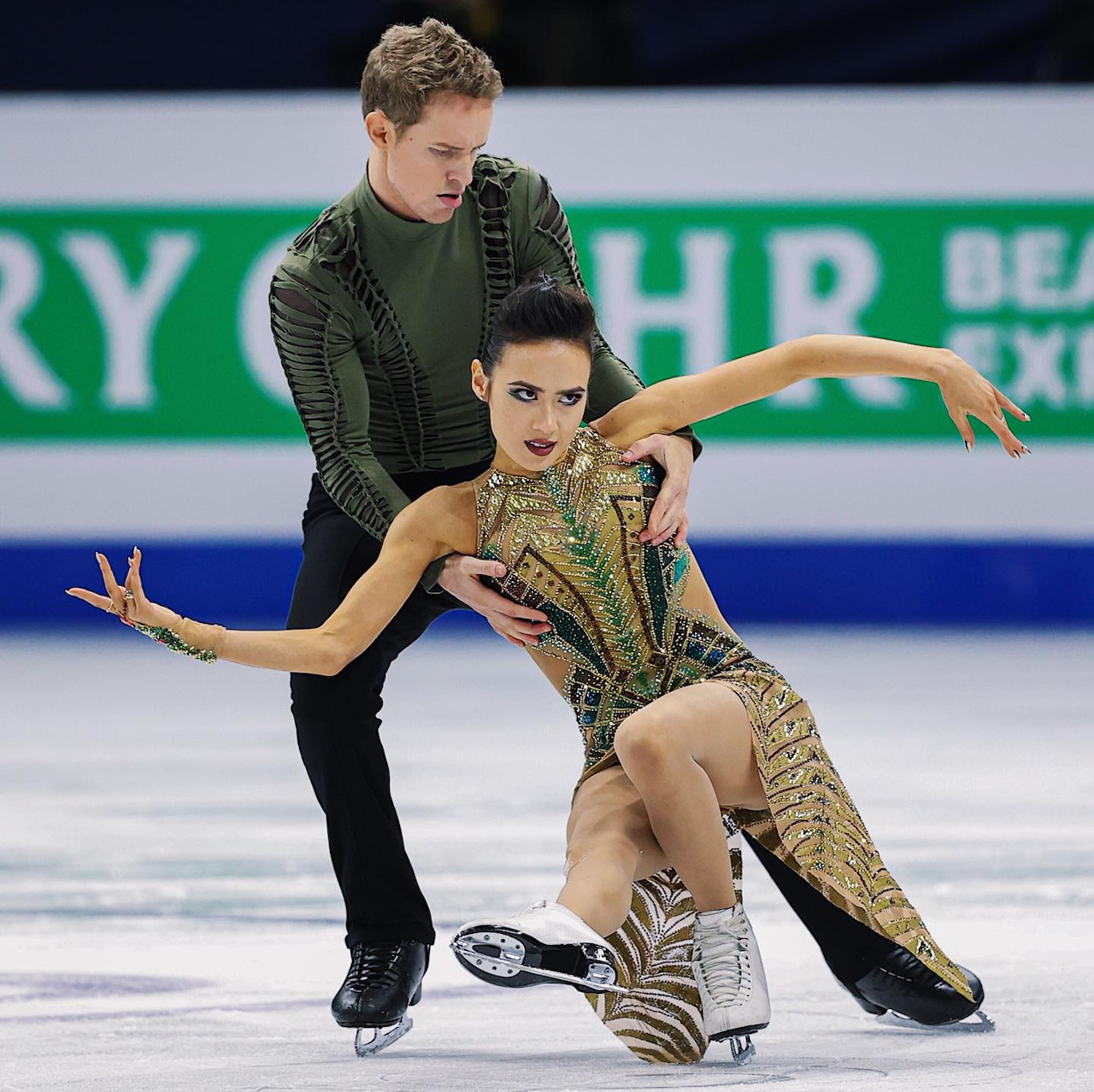 Figure skating pair performing ice dance routine in matching green costumes on indoor rink