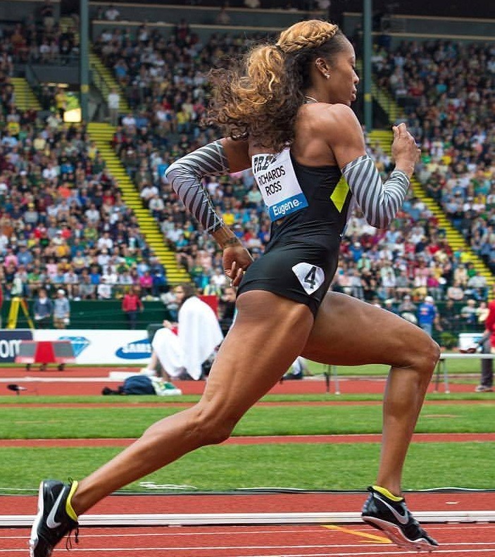 Female athlete running at full speed on an outdoor track in a crowded stadium