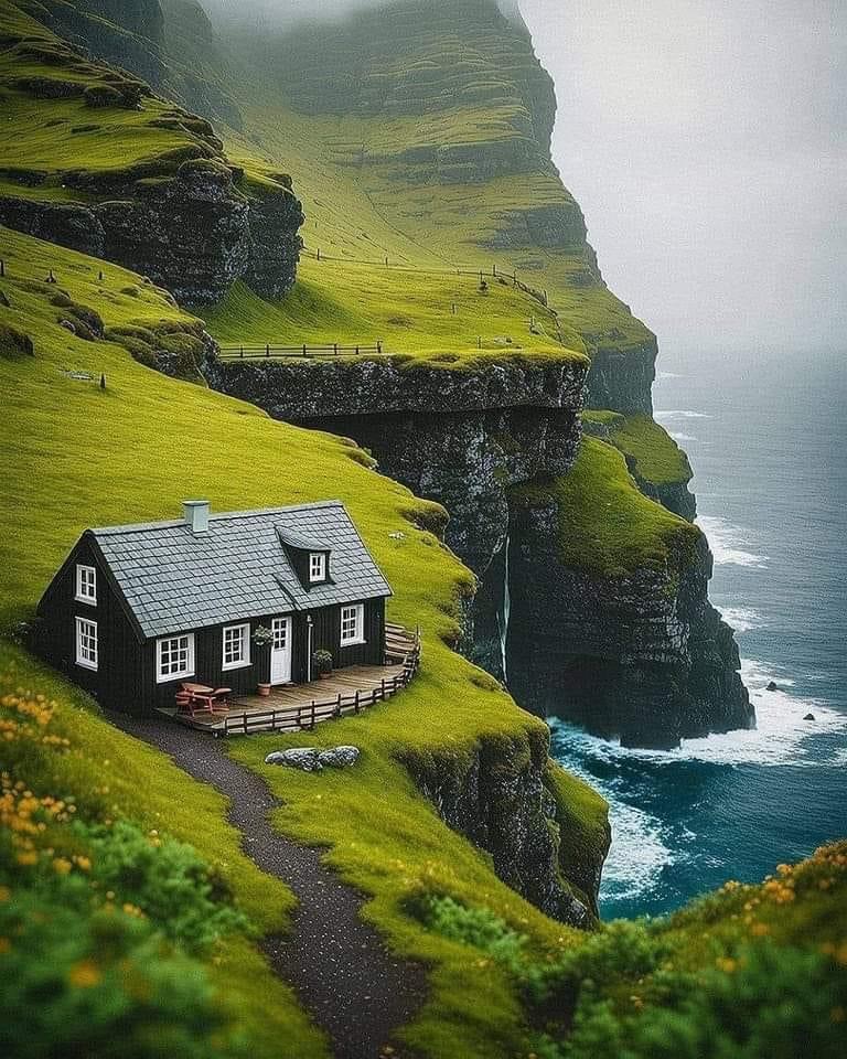 Black house perched on green cliff edge above ocean in Faroe Islands