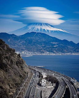 Curved coastal highway in Japan with Mount Fuji topped by a lenticular cloud in the background