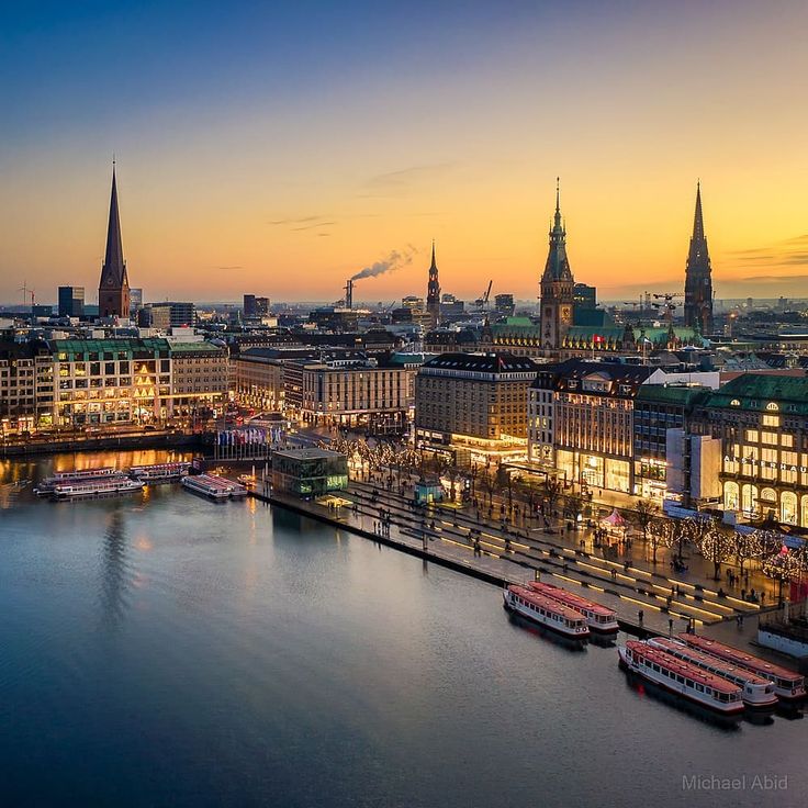 Hamburg city skyline at sunset with waterfront, historic spires, and glowing buildings reflected in water