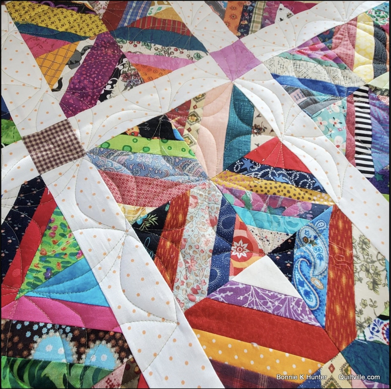 Colorful patchwork quilt with triangular fabric pieces in geometric pattern separated by white lattice