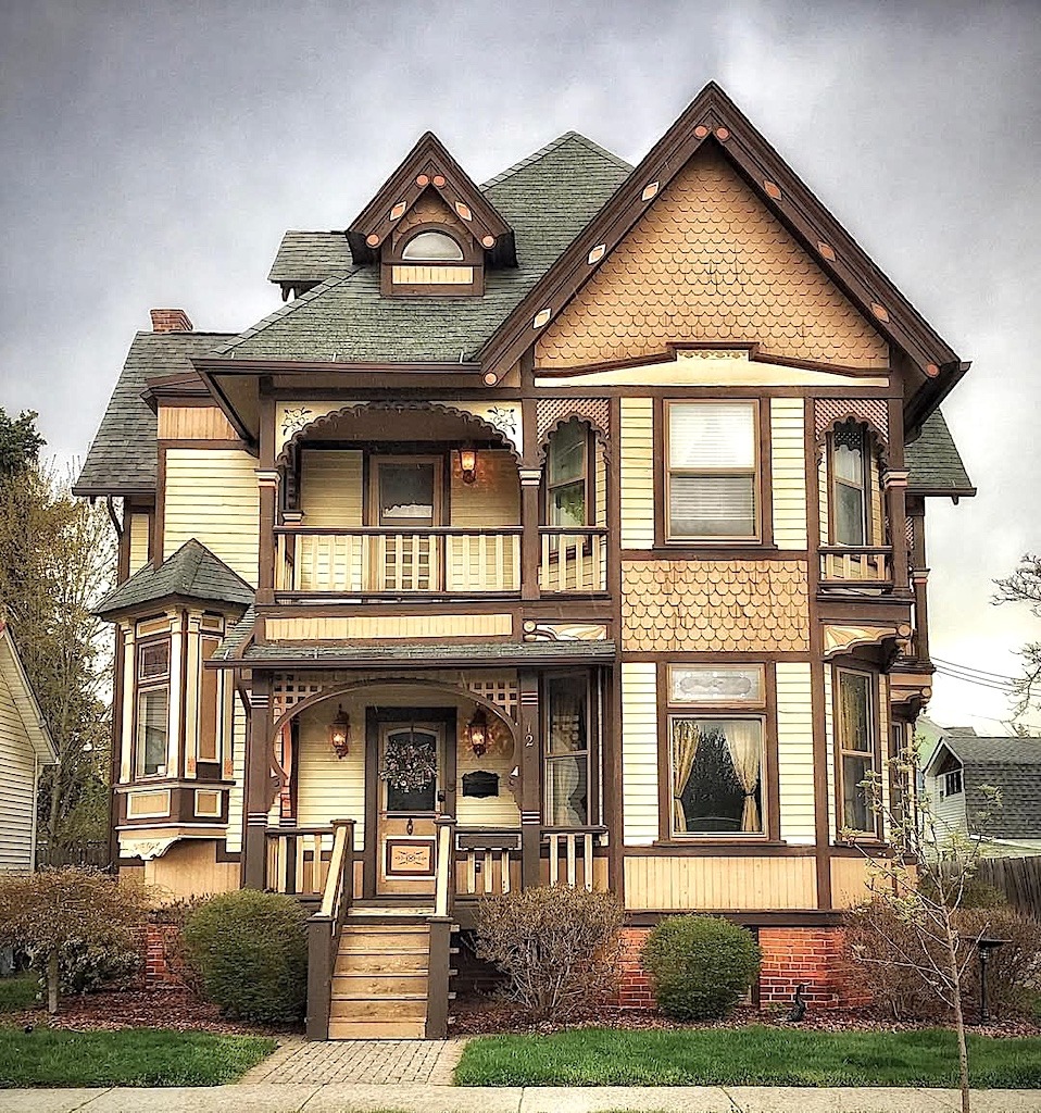 Two-story Victorian house with wraparound porch, ornate trim, turret, and cream-colored siding