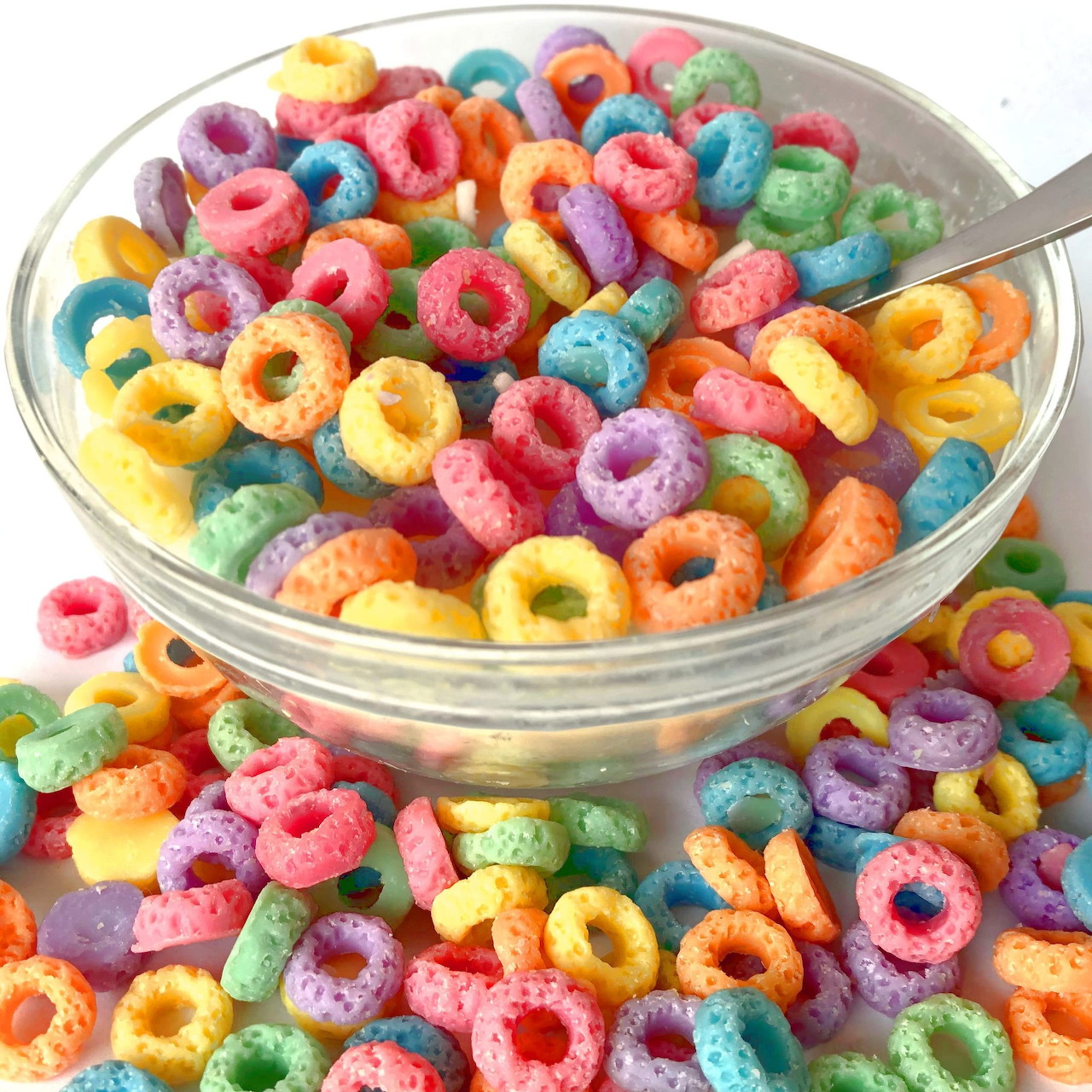 Bowl of colorful Froot Loops cereal in milk with spoon, cereal scattered around bowl on white background