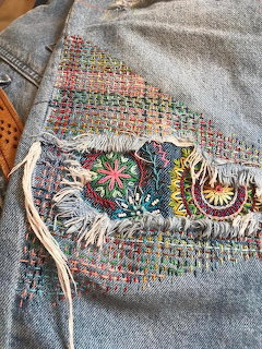 Denim pocket with colorful embroidered flowers and decorative stitching on light blue jean fabric