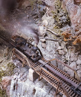 Model steam train crossing a wooden trestle bridge in a detailed miniature mountain diorama