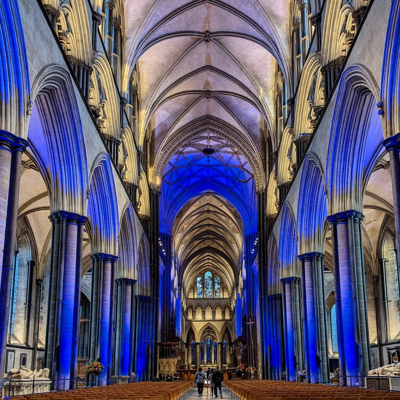 Interior view of Salisbury Cathedral showing Gothic arches, vaulted ceiling, and blue illuminated columns