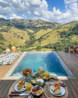 Infinity pool with breakfast table on deck overlooking lush mountain valley