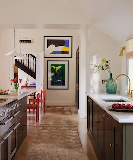 Galey kitchen with dark cabinets, white countertops, red chairs, artwork on walls, and staircase in background
