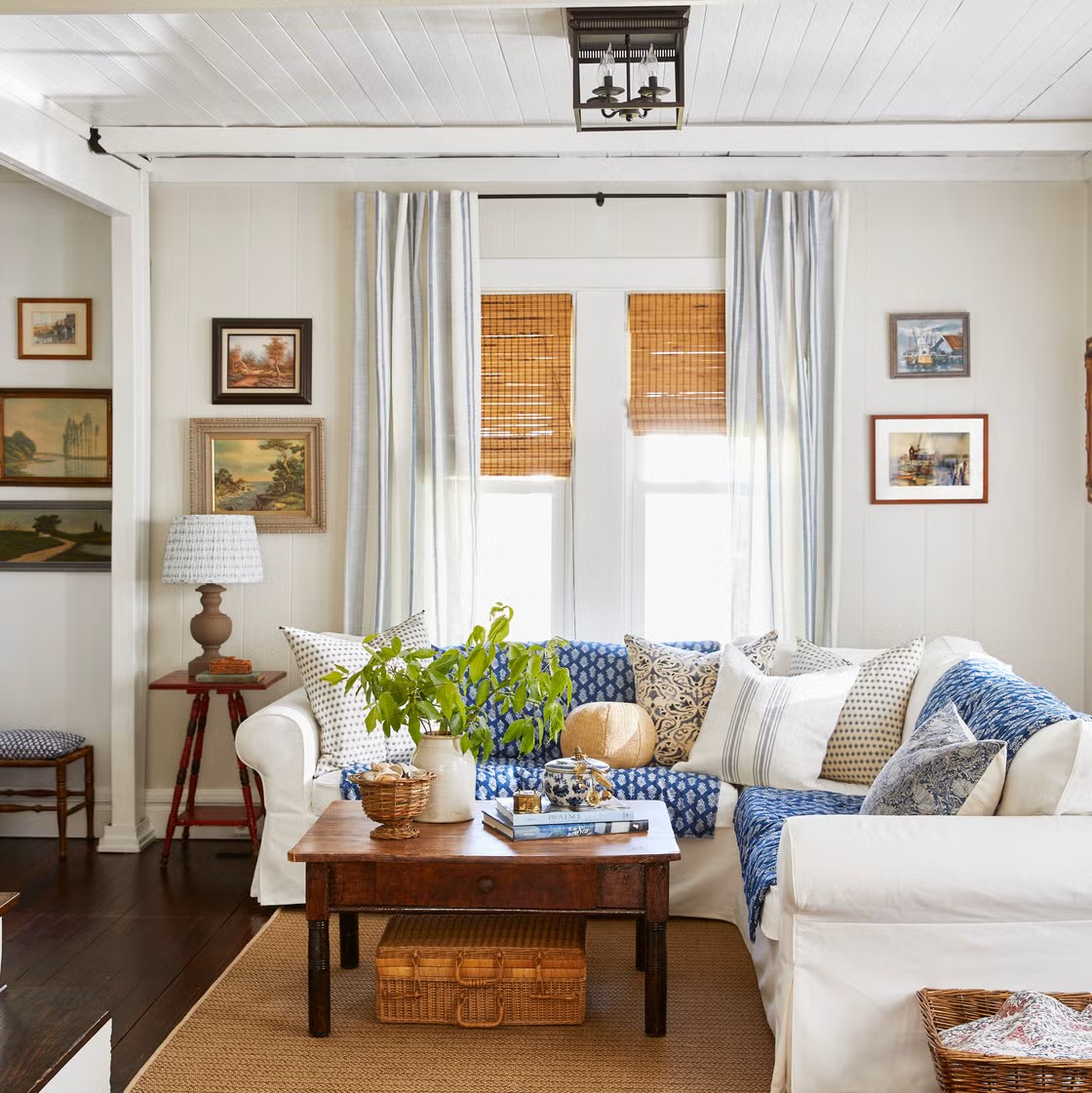 Cozy cottage living room with white couch, blue accent pillows, wood table, and natural light from windows