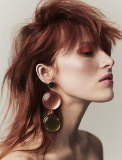 Profile view of a redhead woman with mesy hair wearing large round drop earrings