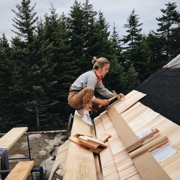 Worker laying wooden shingles on roof with forest backdrop