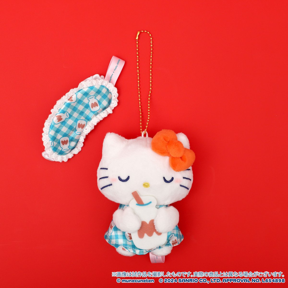 Hello Kitty plush keychain with orange bow and blue gingham outfit holding a drink, next to a sleep mask on red background