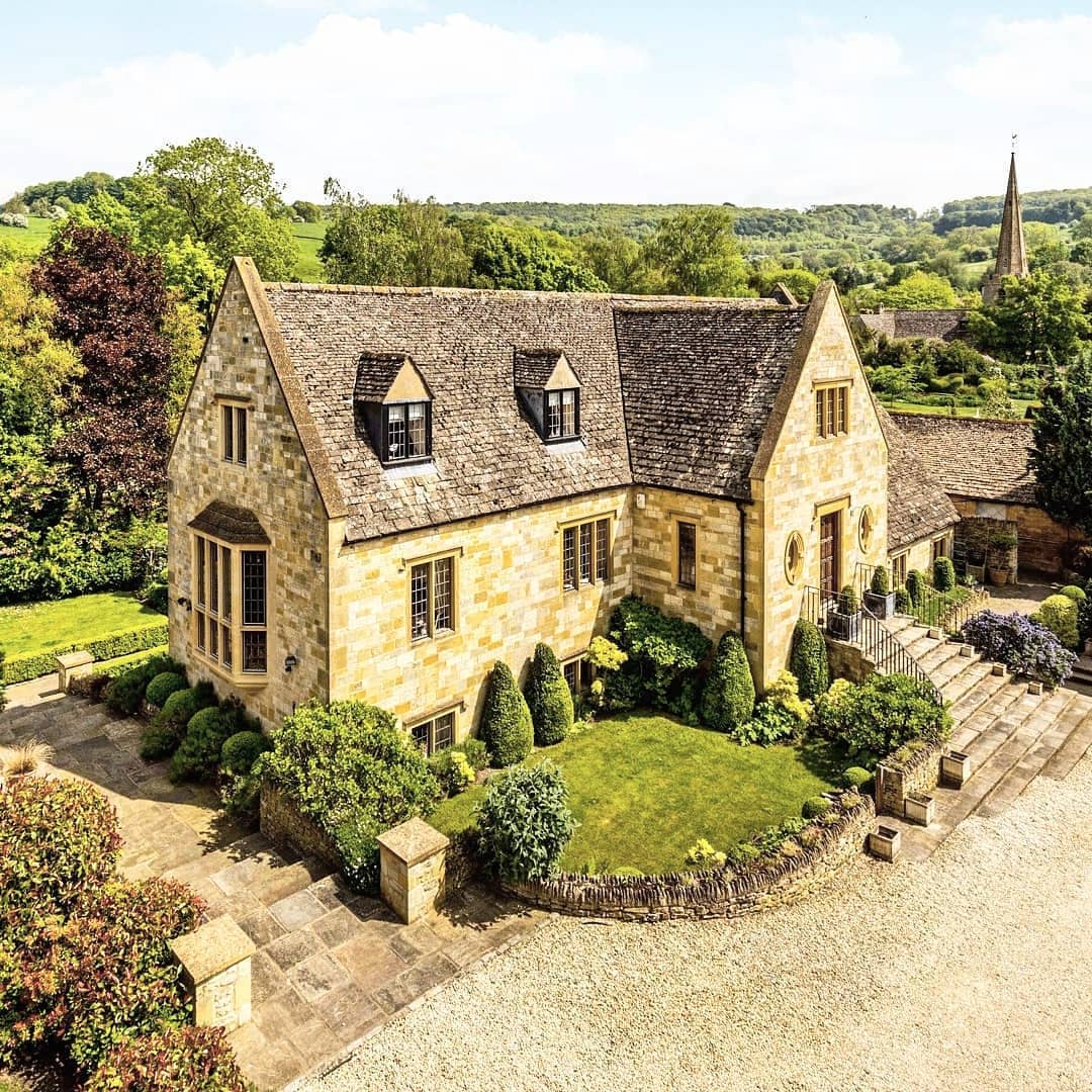 Aerial view of traditional Cotswolds stone house with garden and gravel driveway in English countryside
