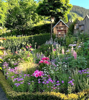 Colorful summer garden with flowering plants and wooden insect hotel structure among pink and purple flowers