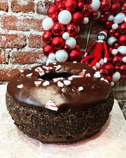 Large chocolate donut cake with peppermint pieces on top, Christmas ornament wreath andelf on shelf in background