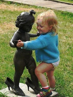 Toddler in blue sweater dancing with bronze child statue on grass