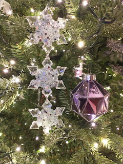 Snowflake ornaments and a purple bauble on a Christmas tree with warm lights