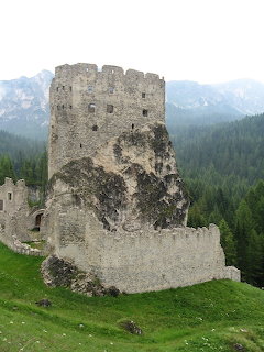 Ruins of Castello di Andraz on a grassy hill with forest and mountains behind