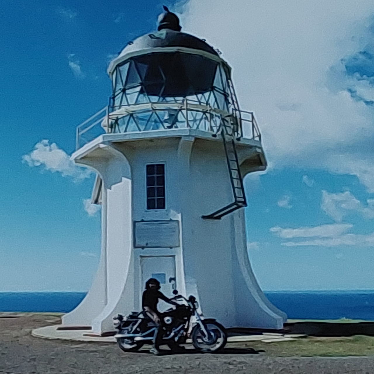 White lighthouse with a motorcycle in front beside the sea under a blue sky