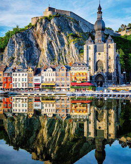 Historic town of Dinant with cliff-top citadel and church reflected in calm river water