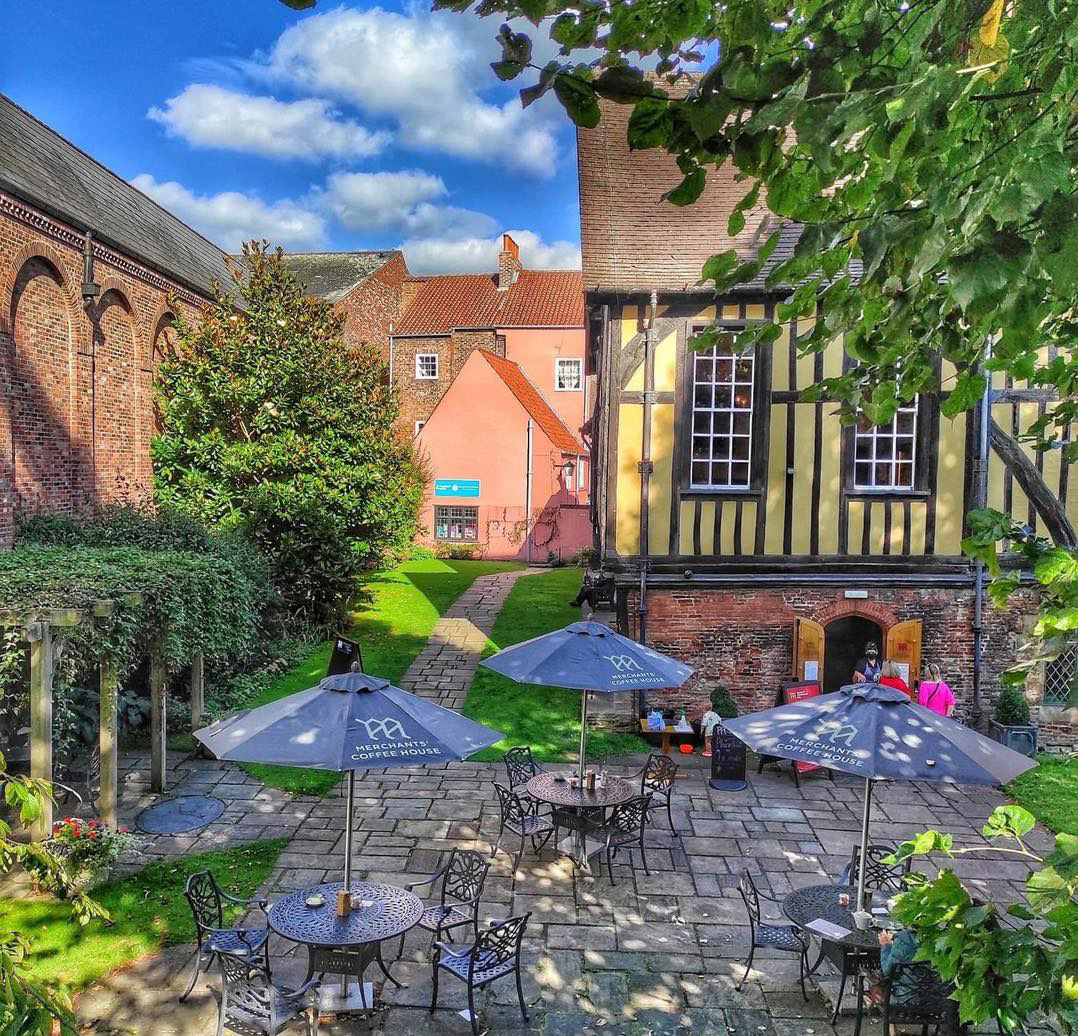 Courtyard patio next to a historic timber-framed hall with garden plants, tables, and umbrellas