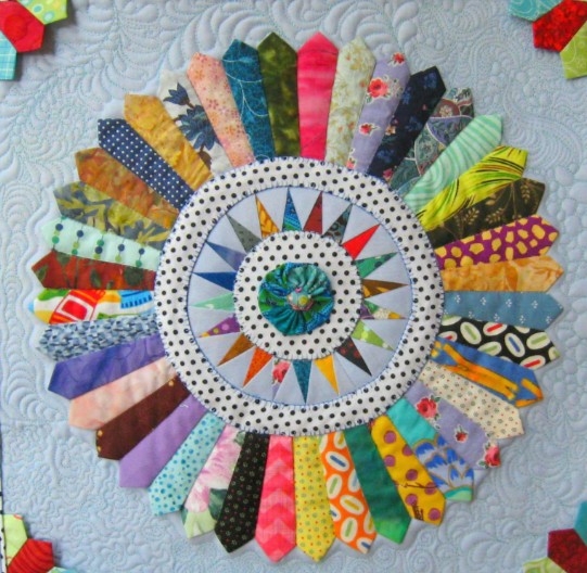 Dresden plate quilt block with colorful patterned fabric wedges arranged in circle on light blue background