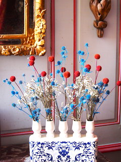 Dried flower arrangement with red and blue blooms in white vases on decorative blue and white ceramic stand