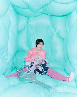 Woman in pink outfit sitting in an aqua inflatable room holding an open magazine