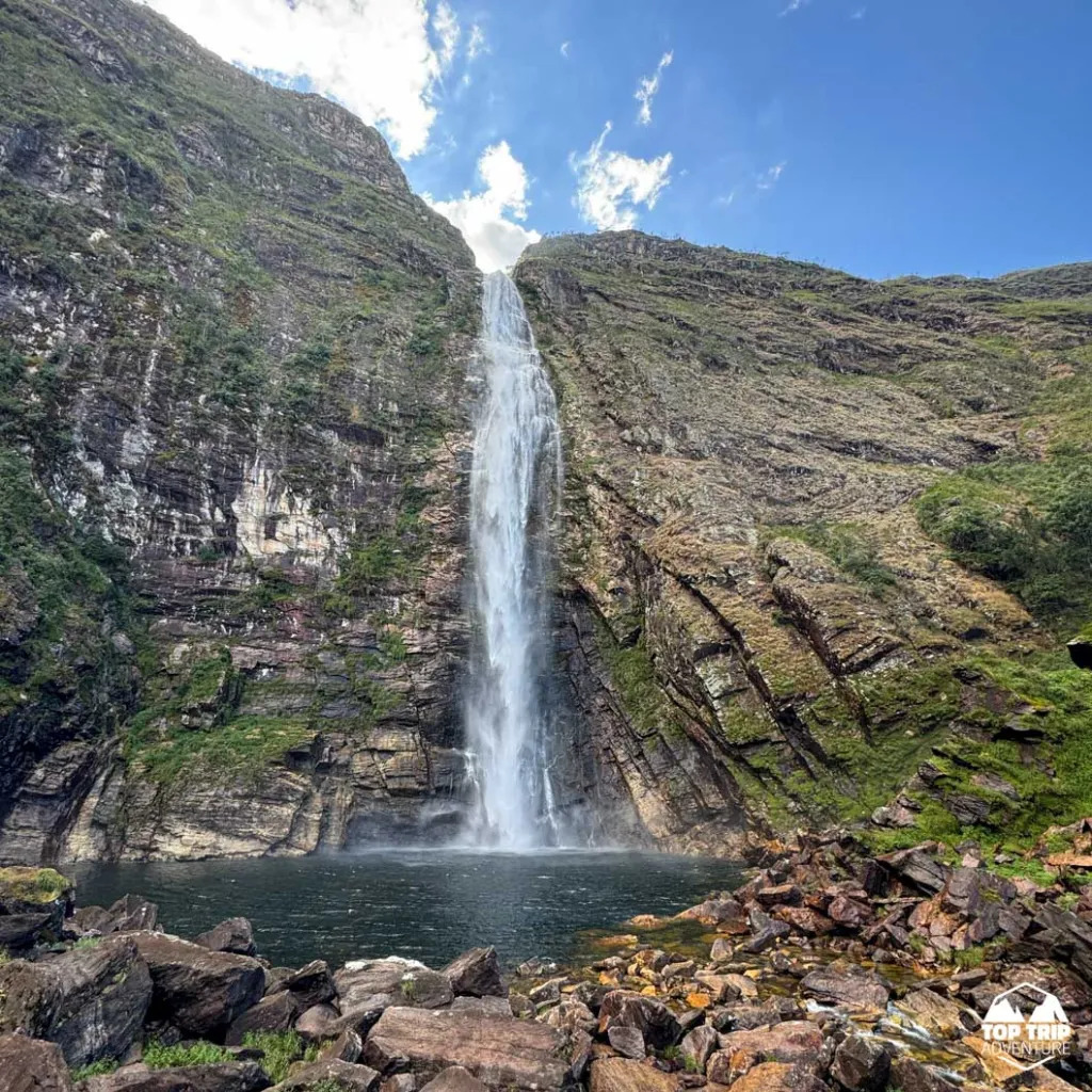 Waterfall falling down a rocky cliff into a pool with stones in the foreground