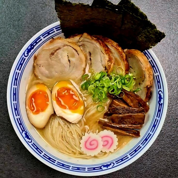 Bowl of ramen with pork slices, soft-boiled eggs, green onions, seaweed, mushrooms, and fish cake