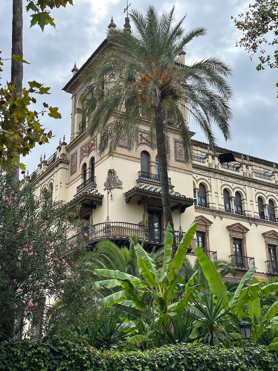 Ornate historic building in Seville with palm trees and lush gardens in foreground
