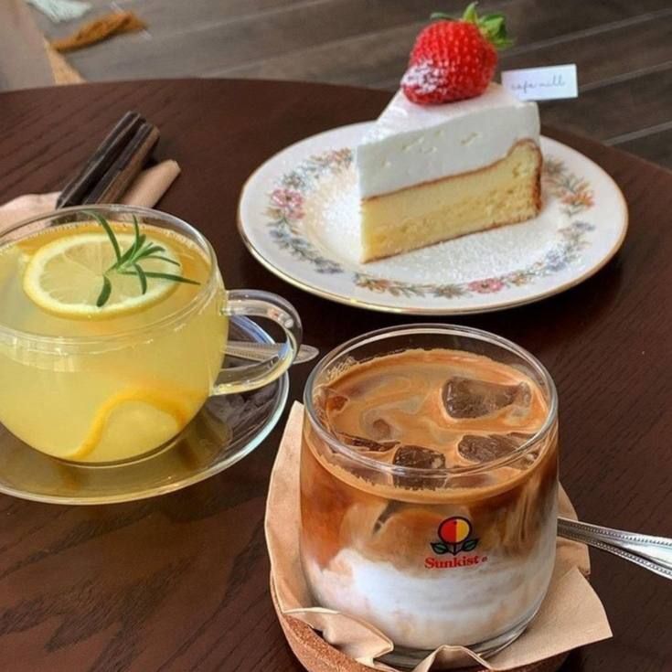 Slice of strawberry cream cake with an iced latte and a yellow citrus drink on a wooden table