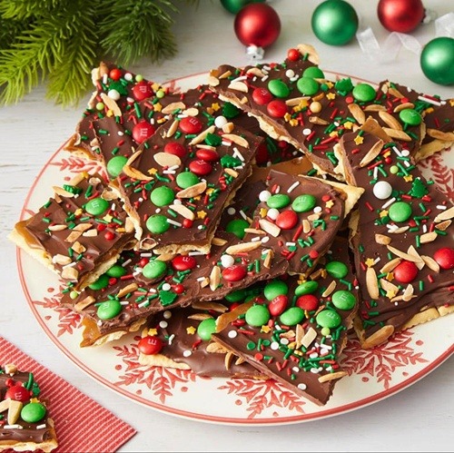 Chocolate bark with colorful candies and nuts on festive plate with ornaments