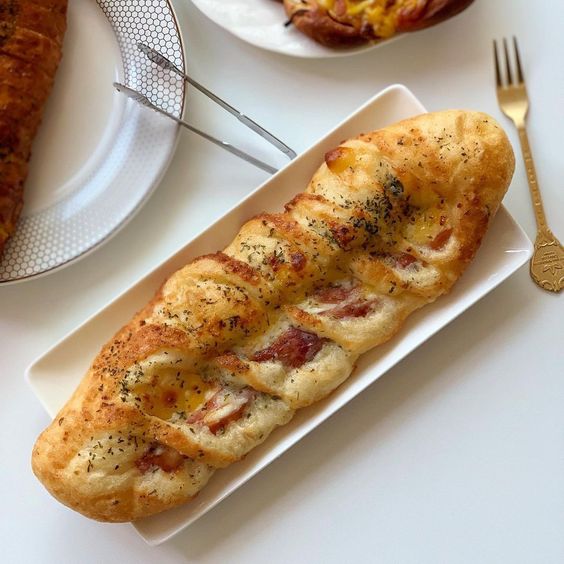 Braided baked bread loaf with herb topping on a white rectangular plate
