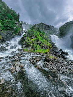 Twin waterfalls flowing over rocky mountain cliffs surrounded by lush green vegetation under dramatic cloudy sky