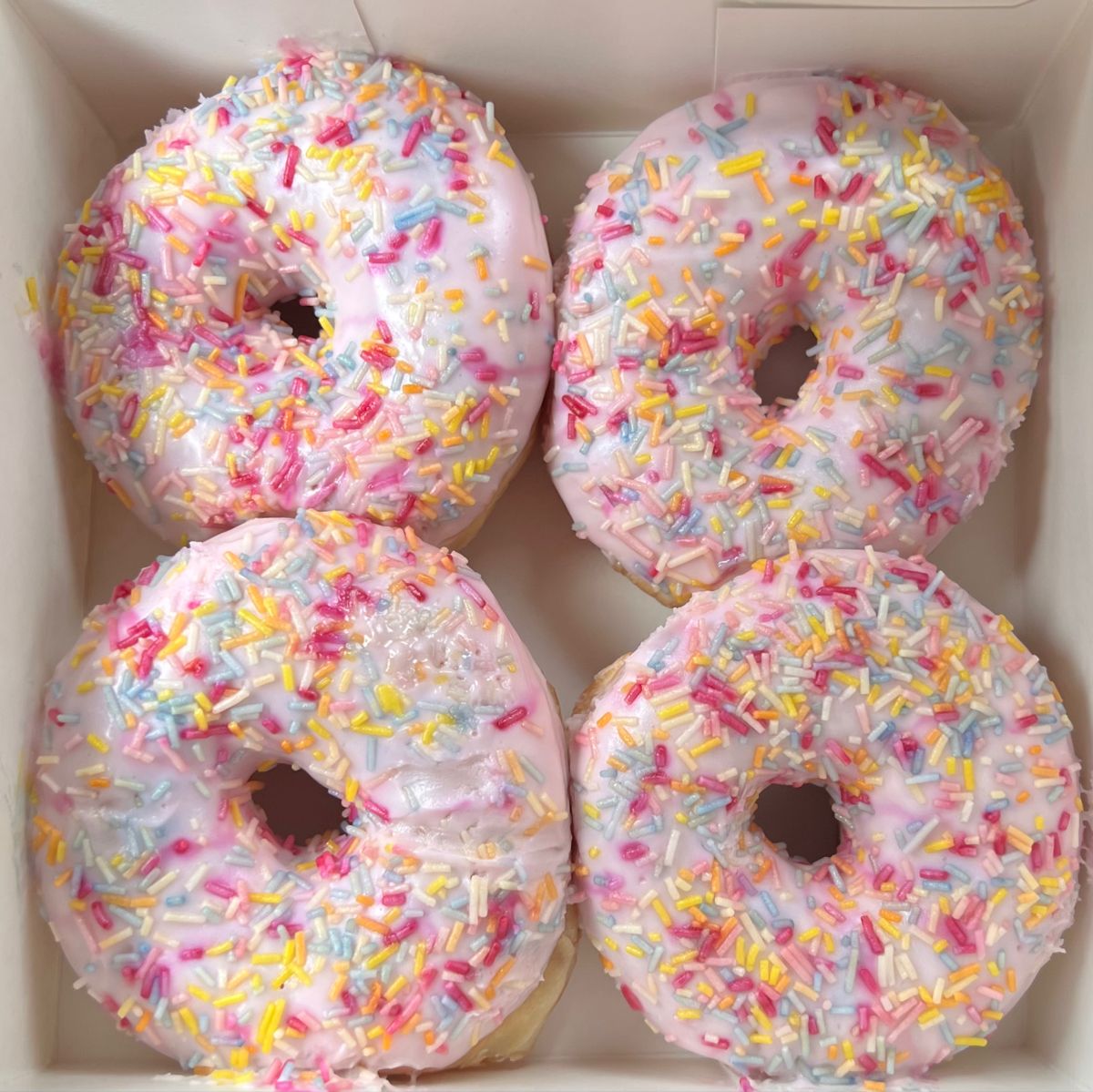 Four frosted donuts with rainbow sprinkles in white box