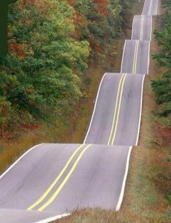 Winding road curving through green mountains under a bright sky