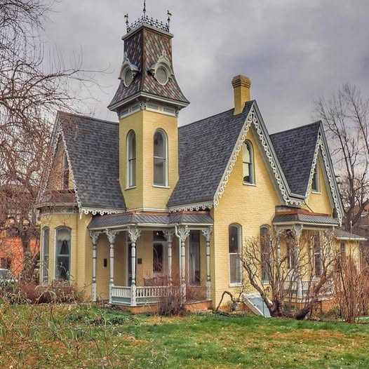 Yellow Victorian house with ornate tower and white trim against overcast sky